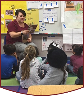 Teacher reading to students as they sit on the classroom floor